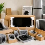 Packed fragile electronics including TV, laptop, gaming console, and appliances prepared safely for home relocation in India.